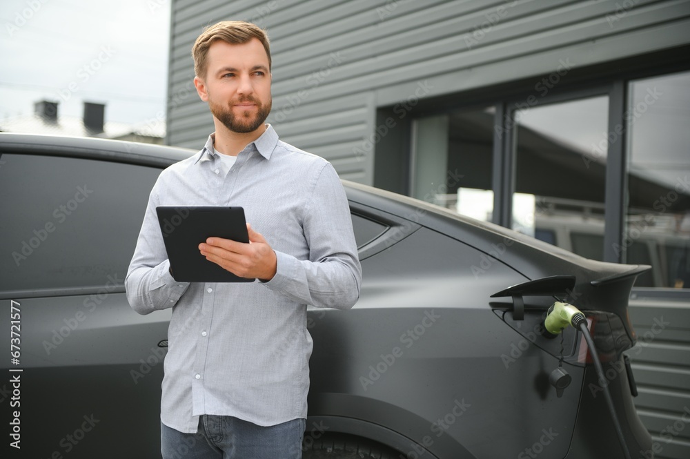 Fototapeta premium A man charges his modern electric car. The concept of green energy