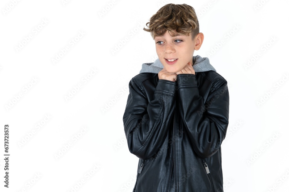 caucasian kid boy wearing black jacket holds hands under chin, glad to hear heartwarming words from stranger caucasian kid boy wearing black jacket holds hands under chin, glad to hear heartwarming words from stranger
