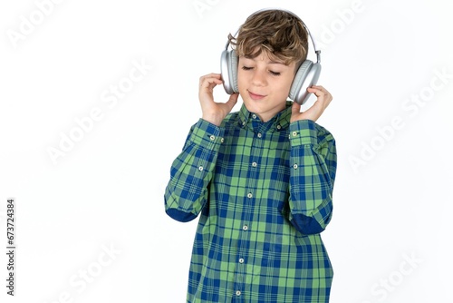 Pleased caucasian kid boy wearing plaid shirt enjoys listening pleasant melody keeps hands on stereo headphones closes eyes. Spending free time with music