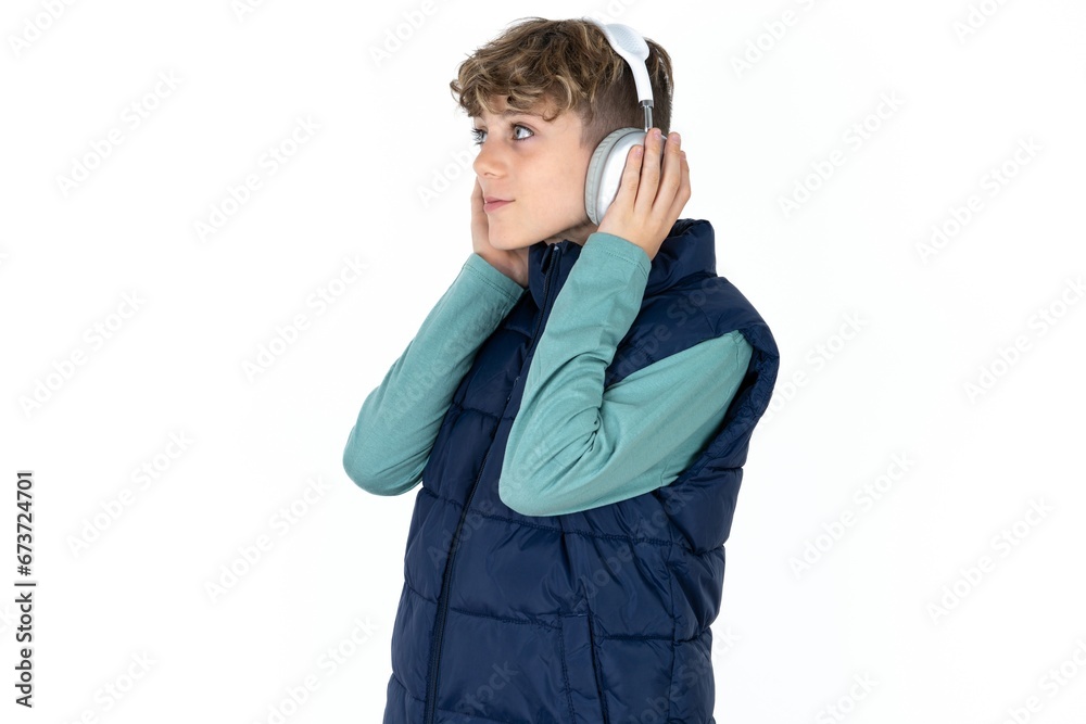 caucasian kid boy wearing blue vest wears stereo headphones listens music concentrated aside. People hobby lifestyle concept caucasian kid boy wearing blue vest wears stereo headphones listens music concentrated aside. People hobby lifestyle concept