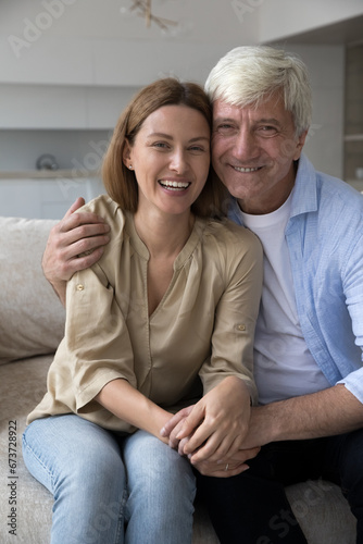 Funny family self portrait of cheerful senior dad and pretty adult daughter child holding device in hand, smiling at camera, laughing, taking home selfie making video call, showing victory fingers