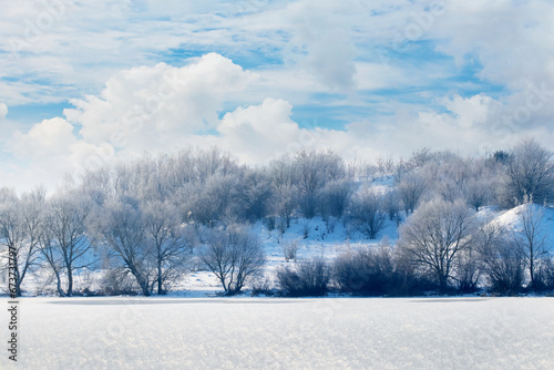 Winter landscape with trees on the banks of the river and a picturesque blue sky with white curly clouds in sunny weather © Volodymyr