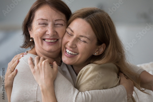 Happy older mature mom and pretty daughter child hugging with love, affection, enjoying bonding, closeness, relationship, meeting, looking at camera, smiling, laughing. Family portrait