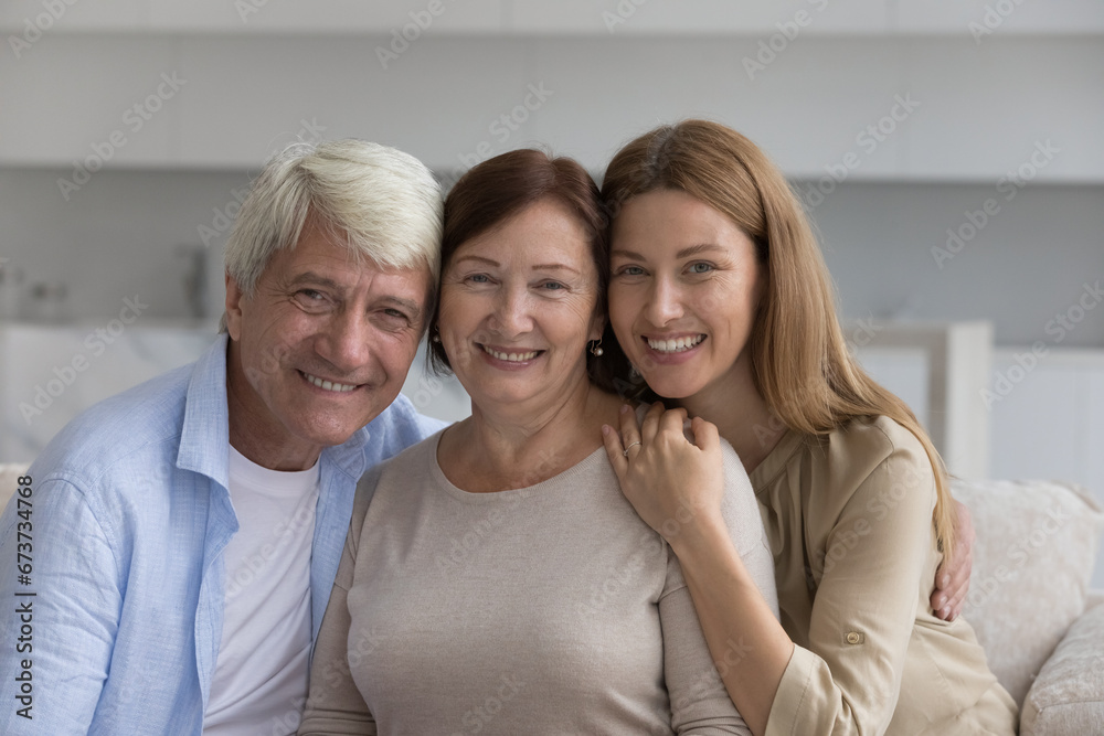 Φωτογραφία Older man posing for family portrait, hugging mature senior wife and adult daughter, looking at camera, smiling