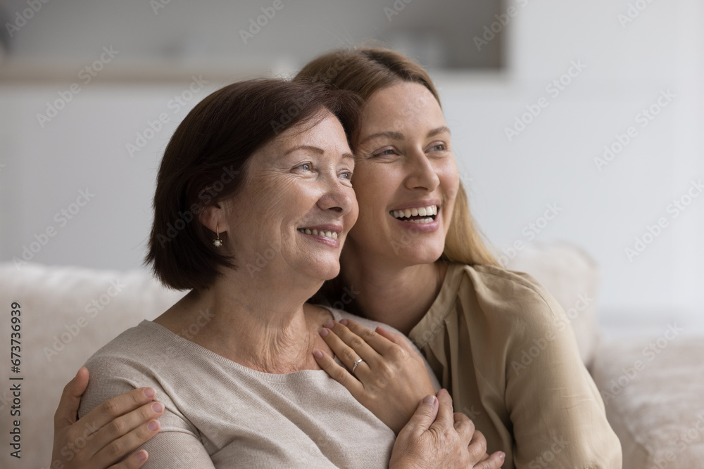 Cheerful pretty mature mom embracing, cuddling daughter on home couch, laughing, hugging adult child with love, affection, tenderness, happiness, smiling, enjoying family bonding, relation Cheerful pretty mature mom embracing, cuddling daughter on home couch, laughing, hugging adult child with love, affection, tenderness, happiness, smiling, enjoying family bonding, relation