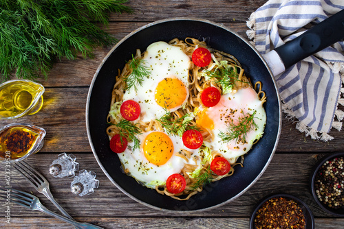 Fried eggs on noodles with fresh vegetables in frying pan
 photo