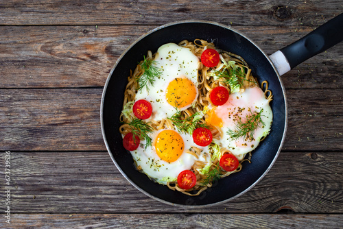 Fried eggs on noodles with fresh vegetables in frying pan 