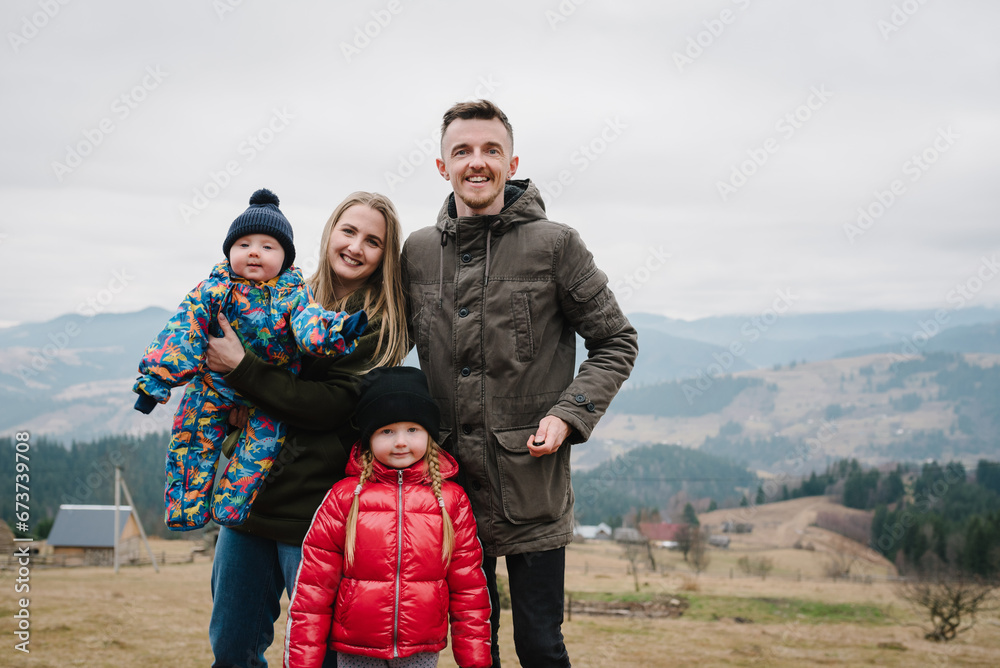 Mother, father embrace kids on terrace on an autumn day. Family vacation with children in mountains. People relax in country. Mom, dad hug daughter, son enjoy time together. Weekend, travel concept