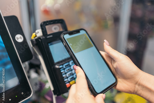 Hands of unrecognizable young woman making electronic payment with her mobile phone. Digital payment made with a smartphone at a supermarket self-service express checkout POS. photo