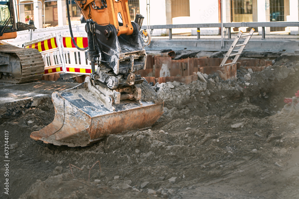 Fototapeta premium Close-up of big excavator on the urban construction site. Modern construction machinery at a construction site. Isolated scoop close up. Road construction. Architecture, engineering.
