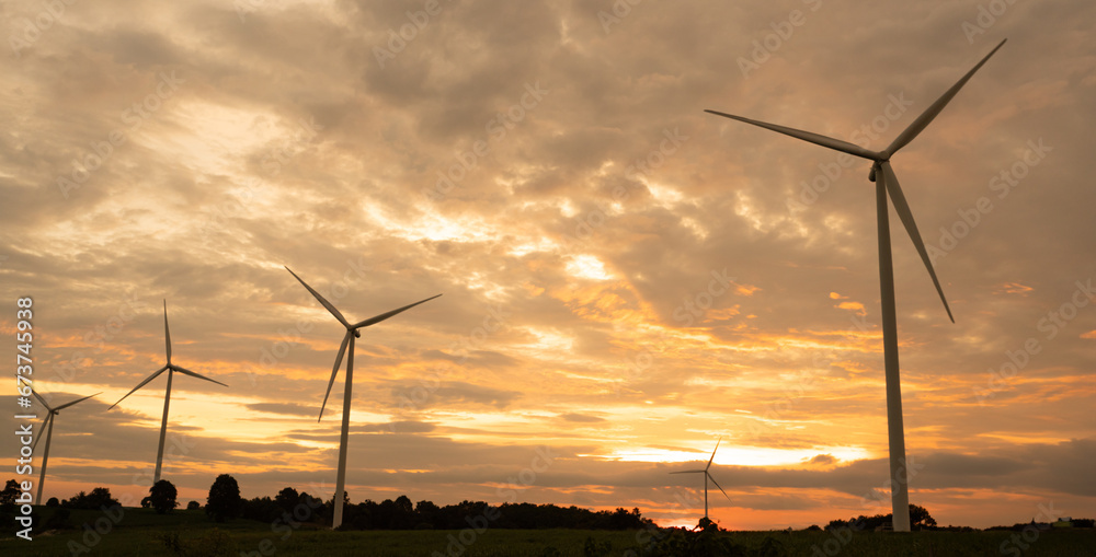 Obraz premium Wind turbines generate electricity in a rural area during sunset. Windmill farm on mountain with sunset sky. Wind energy, renewable energy, Green technology.
