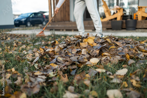 cropped view of man cleaning fallen leaves from lawn with broom in yard