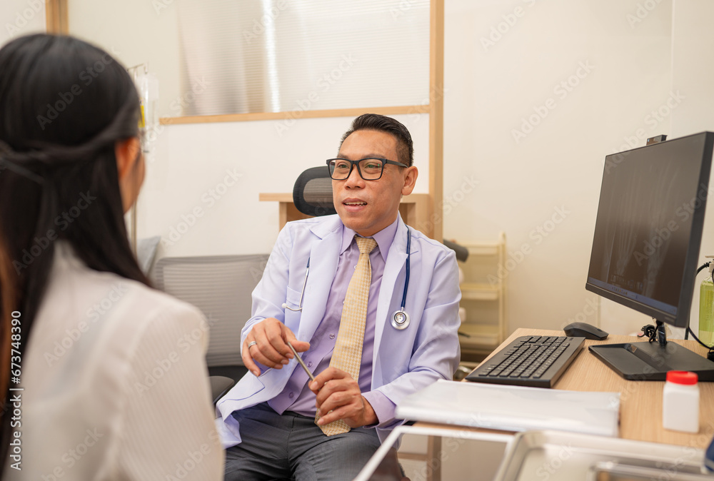 Fototapeta premium Mature male doctor explain to the woman patient the result of x-ray that show fracture of her calcaneus. Doctor Showing X-ray To Patient On Computer Screen.