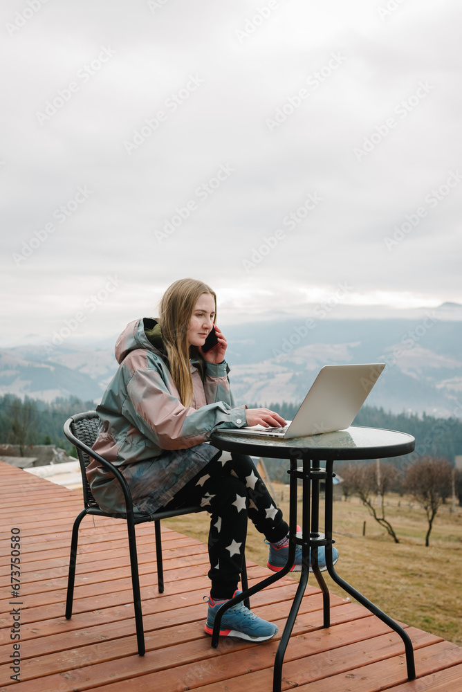 Female talking on phone outdoors. Woman remote work on laptop sitting table with great view mountains. Workplace in country in backyard house in morning. Concept freelance lifestyle. Internet 5G. Female talking on phone outdoors. Woman remote work on laptop sitting table with great view mountains. Workplace in country in backyard house in morning. Concept freelance lifestyle. Internet 5G.