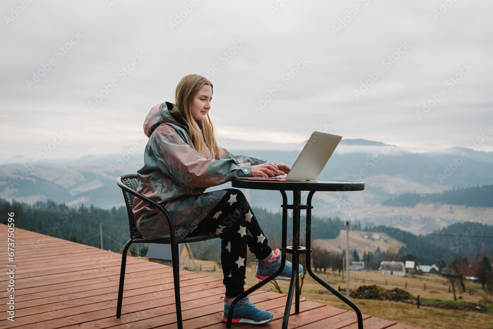 Female working with a great view mountains. Workplace in country in backyard house in morning. Woman remote work on laptop at sitting at a table outdoors. Concept freelance lifestyle. Internet 5G. Female working with a great view mountains. Workplace in country in backyard house in morning. Woman remote work on laptop at sitting at a table outdoors. Concept freelance lifestyle. Internet 5G.