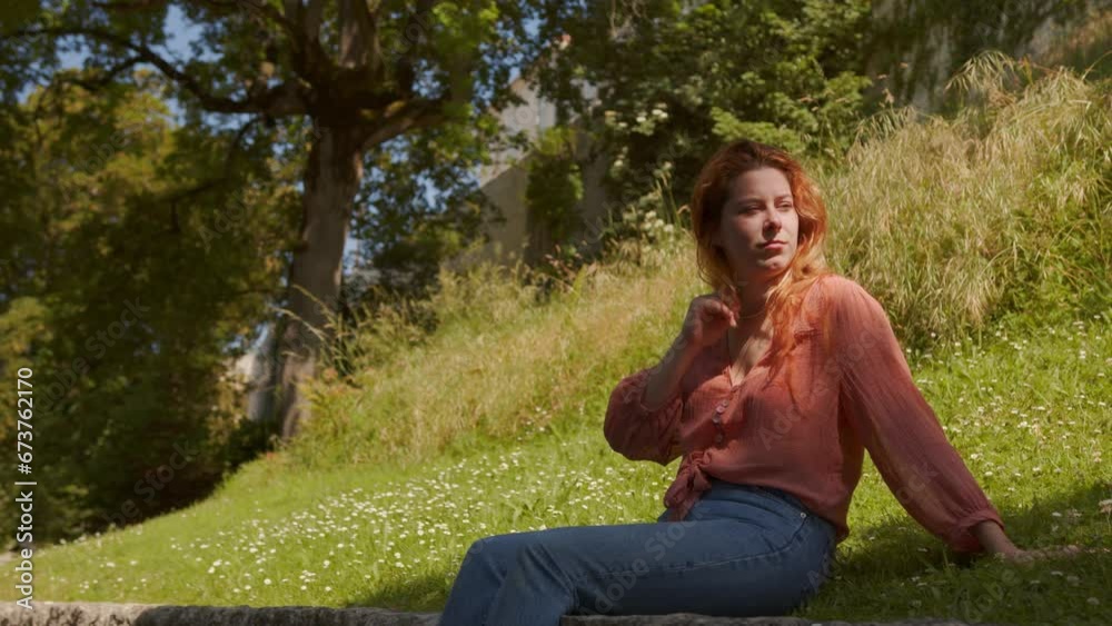 Attractive Red Head Lady Sitting And Relaxing On Grass At The Park. static Attractive Red Head Lady Sitting And Relaxing On Grass At The Park. static