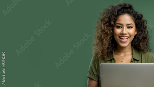 Young happy Latin woman winner holding a laptop isolated on a green background. Excited euphoric female model using computer winning online celebrating new great job offer with yes gesture concept. photo
