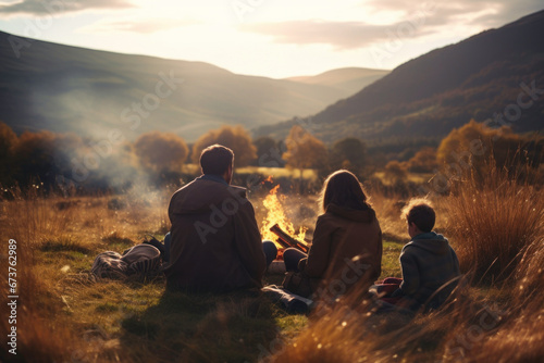 Family sitting at campfire in evening during mountain trip. People having fun sitting at bonfire looking at mountain landscape. Family time. Weekend trip