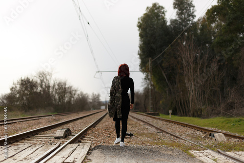 En las vías del tren una mujer caminando con chaqueta militar de espaldas,  © Imagen Punto de Luz