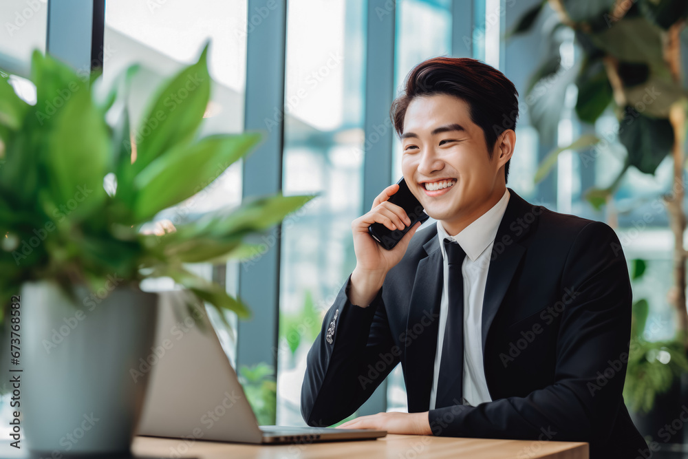 Asian business man smiling and holding cellphone, making a business call. Portrait of confident young man in suit smiling at camera. Business concept