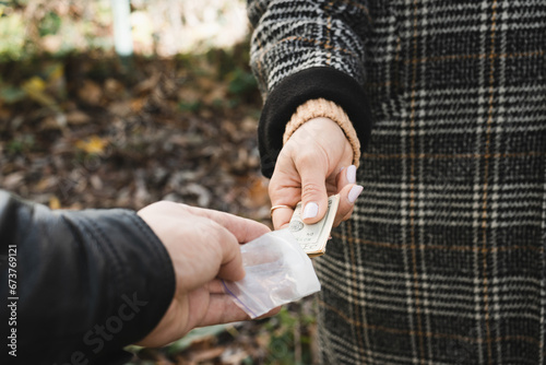 Male drug dealer sells hard drugs in a transparent plastic bag to an addicted woman with money in her hand, cropped image photo
