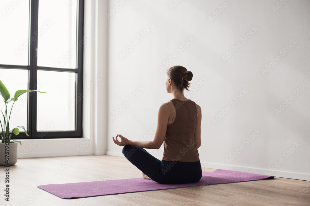 Young woman practicing yoga near floor window in yoga studio, Young girl meditating at home, Harmony, balance, meditation, relaxation, healthy lifestyle concept - obrazy, fototapety, plakaty 