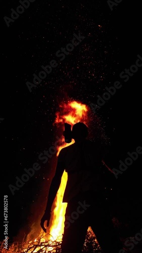 dark silhouette of a man with a fire axe on the background of a beautiful bonfire with particles of sparks, vertical 4K