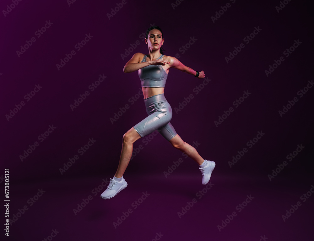Full length of slim woman in silver sports clothes running and jumping over a magenta backdrop Full length of slim woman in silver sports clothes running and jumping over a magenta backdrop