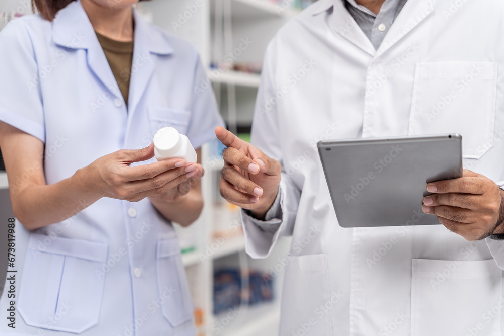 Close up of asian male pharmacist and coworker wearing lab coat and checking medicine product stock with database tablet in the pharmacy drugstore. Close up of asian male pharmacist and coworker wearing lab coat and checking medicine product stock with database tablet in the pharmacy drugstore.