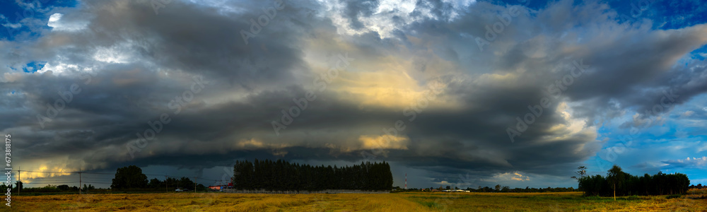 Panorama Photo of Super storm with sun light , Dark sunset sky and dramatic black cloud before rain.rainy storm over rice fields,countryside Thailand,ASIA.