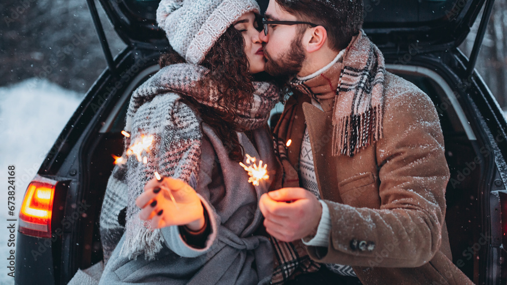 Romantic couple in love celebrate together the new year with fire sparkler at the back of car. Love is in the air. Christmas time.