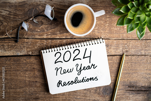 New year resolutions 2024 on desk. 2024 goals list with notebook, coffee cup, plant on wooden table. Resolutions, plan, goals, action, checklist, idea concept. New Year 2024 resolutions. Copy space photo
