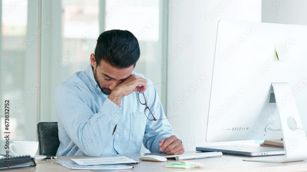Tired and stressed man with a headache sitting alone at his desk inside an office. Exhausted businessman in pain while typing on a computer and wearing glasses, working late and looking overworked Tired and stressed man with a headache sitting alone at his desk inside an office. Exhausted businessman in pain while typing on a computer and wearing glasses, working late and looking overworked