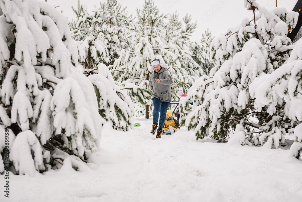 Dad pulling little son on winter day. Children are rolling down hill on sledge in forest. Happy funny child with father ride sled on snowy road in mountains. Family walks during snowfall in park.