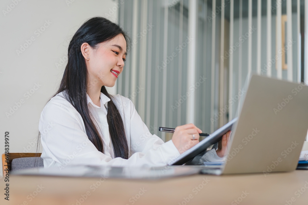 Successful Asian businesswoman looks confident and smiles while working with laptop in office. Successful Asian businesswoman looks confident and smiles while working with laptop in office.