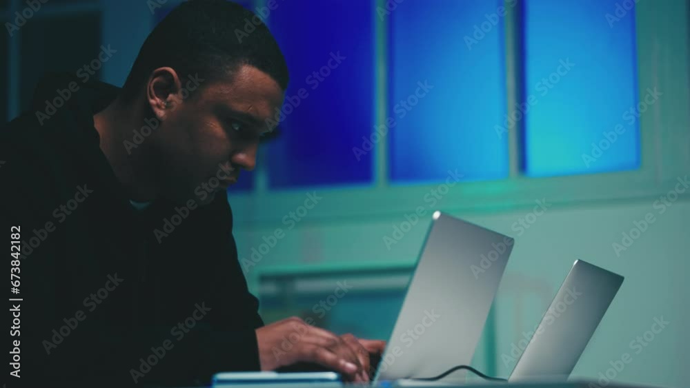 Young African American man creating malware on laptop, hacker working at night Young African American man creating malware on laptop, hacker working at night