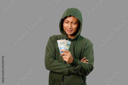 Adult Asian man wearing green hoodie showing happy expression while holding money isolated on gray background. photo