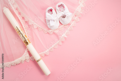 Christening background with baptism baby shoes, dress and candle on pink background. photo