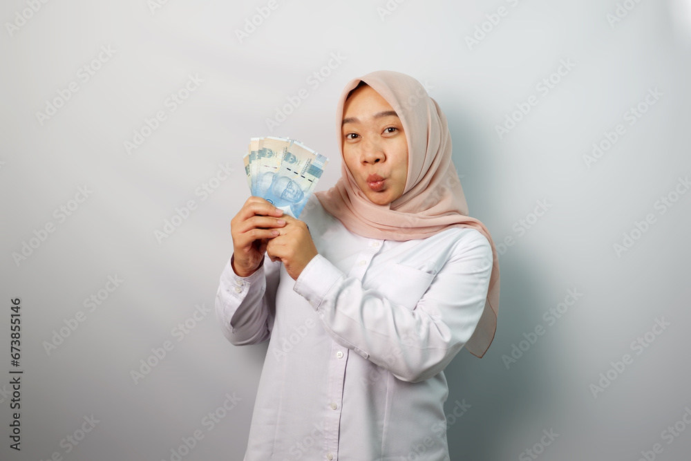 Enthusiastic Asian hijab woman looking excited at camera and holding money rupiah in hand isolated on white background Enthusiastic Asian hijab woman looking excited at camera and holding money rupiah in hand isolated on white background