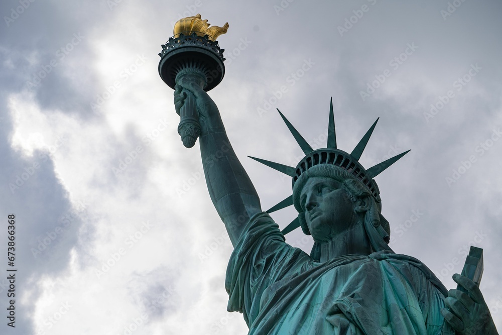Fototapeta premium Majestic Statue of Liberty illuminated against a cloudy sky.