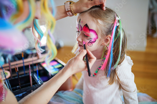 Artist painting little preschooler girl like unicorn on a birthday party. Creative activities for kids photo