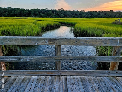Scenic view of a wooden bridge over a river and green meadow on Jekyll Island, Georgia at sunset photo
