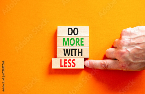 Do more with less symbol. Concept word Do more with less on beautiful wooden block. Beautiful orange table orange background. Businessman hand. Business do more with less concept. Copy space.
