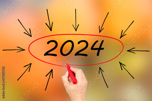 2024, Woman writing the number 2024 on orange background. Happy New Year