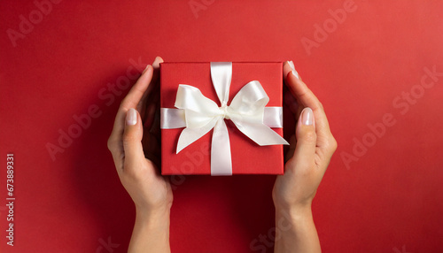 Female hands holding a red gift box on a red background