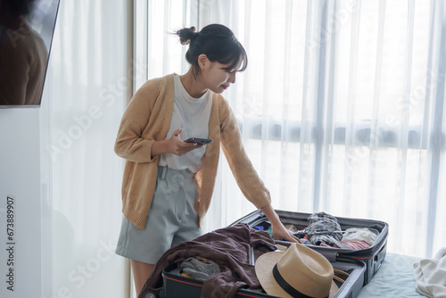 Asian girl preparing vacation in bedroom. Woman doing checklist before holidays trip