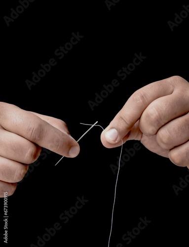 Male hands skillfully threading a needle on a solid black background