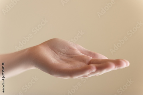 Beautiful woman hand isolated on beige background. Empty open female hand on cream background with copy space. Close up of elegant palm faced upwards with space for your product. Femininity