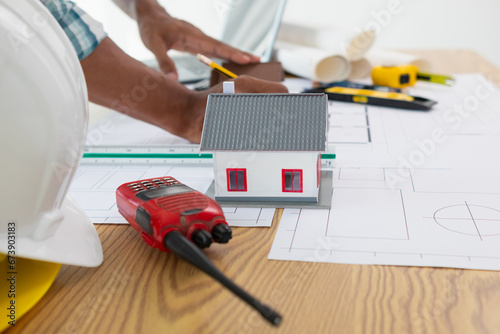 architect is preparing house model and construction plans on blueprints for construction engineering team to review before construction engineering team constructs building according to the drawings.