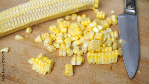 Fresh cooked corn is removed from the stem (cob of corn) using a stenlis knife on a wooden table
 photo